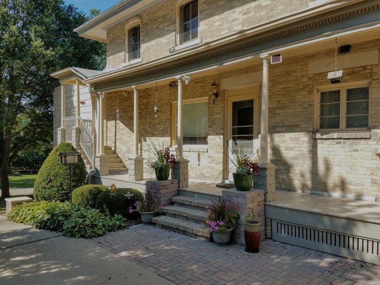 Exterior view of the HA Whitney Inn Bed & Breakfast in Columbus, Wisconsin, showcasing the charming brick facade, side porch, and landscaped entrance with flowers.
