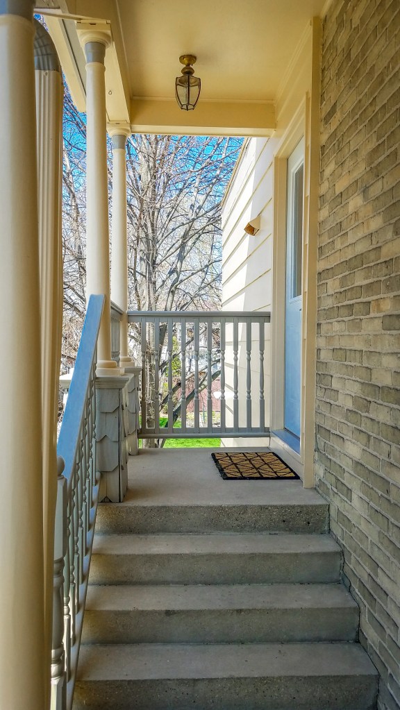 Entrance of the HA Whitney Inn showing stairs leading to the coded private door, with a welcome mat and a view of trees outside.