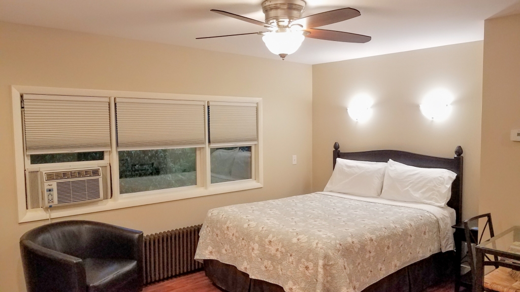 Cozy bedroom in the HA Whitney Inn with a comfy queen bed, a black armchairs, ceiling fan, bedside lights, and guest controlled heat and air conditioning.